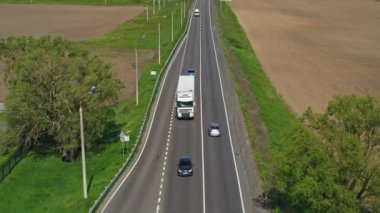 Kamyonlar güneşli bir günde otoyol boyunca araba sürer. Hava takibi atışı. 4K video