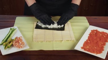 Önlük ve yemek şapkaları, ahşap tahtalar ve hazır vejetaryen malzemelerle birlikte porselen maki yapan kızların zenital görüntüsü..