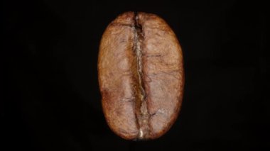 Kahve çekirdeği siyah arka planda dönüyor. Kavrulmuş kahve çekirdeği. Makro. Kahve çekirdeği siyah zemin üzerinde dönüyor. 4K, UHD