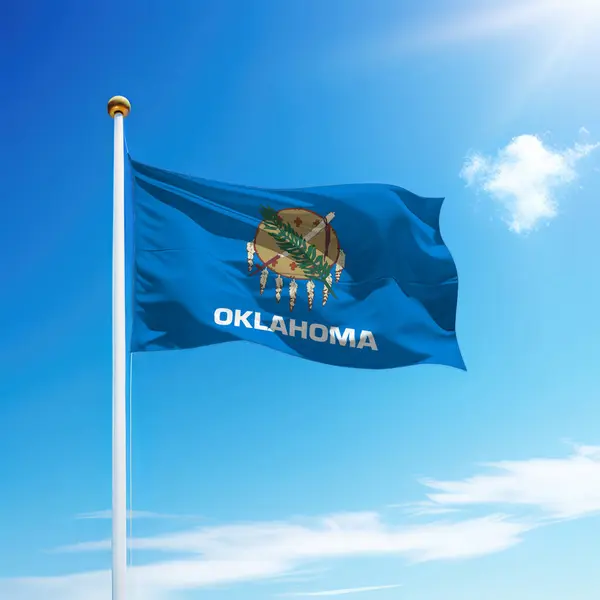 Waving flag of Oklahoma is a state of United States on flagpole with sky background.