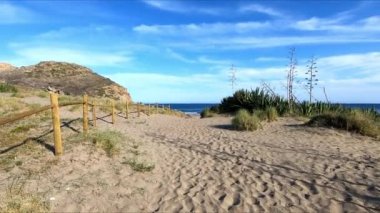 Yaz günü Almerya, Endülüs, İspanya 'da mavi gökyüzü ile huzurlu bir plaja ulaşan kumlu bir yolda yürümek. Görüş Noktası (POV), öznel görünüm