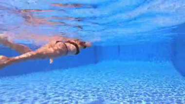 Yüzme stili siyah bikinili, temiz havuzda yüzen kızıl saçlı kadının arkasındaki su altı manzarası. 