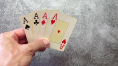 Bir adamın eli desteden dört kartı desenli bir masaya aslarla yerleştiriyor.