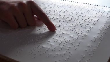 Körler dilinde körler alfabesiyle bir defterden sayfa okuyan bir kızın parmağı: