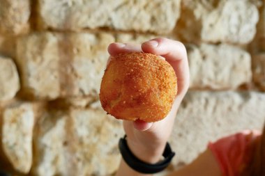 Çocuk eli, büyük küresel bir kroket tutuyor. Lokantanın arka planında taş bir duvar var.