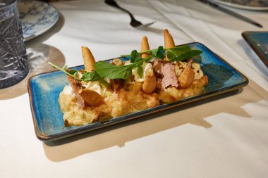 Ton balığı göbekli Rus salatası, mayonez köpüğü, zeytin ve ekmek kalıpları bir restoran masasında ya da evde beyaz bir masa örtüsünde mavi bir tepside.