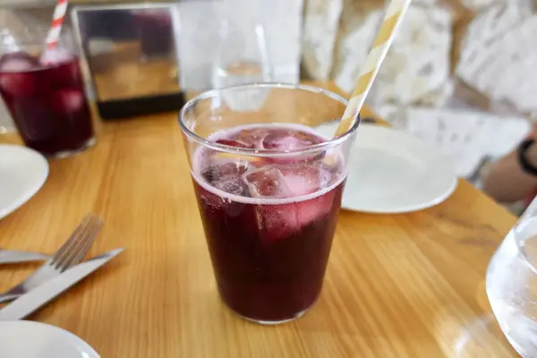 stock image A glass of refreshing sangria or a typical Spanish cocktail with red wine and soda called Tinto de Verano, sits on a wooden table in a restaurant setting. The deep red beverage is filled with ice and garnished with a striped paper straw