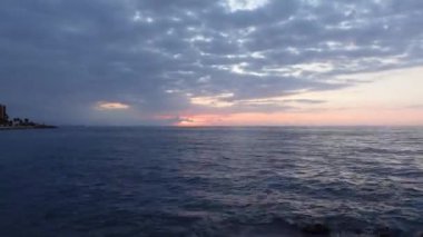 Akdeniz ufkunun suyunun üzerinde mavi saatte bulutlar arasında harika bir gün doğumu zamanı. Gökyüzündeki bulutlar ve okyanus dalgaları hızla hareket ediyor.
