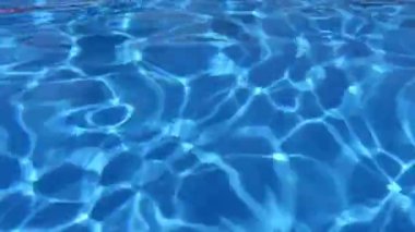 Yüzme havuzundaki canlı mavi su, yüzeyde hafif dalgalanmalar ve yansımalar, dingin ve ferahlatıcı bir su atmosferi oluşturur.