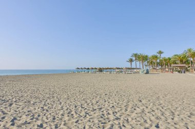 Torremolinos 'taki Los Alamos plajında kumların üzerinde palmiye ağaçları, güneşlik yatakları ve deniz kıyısında saman şemsiyeleri vardı. Malaga, Endülüs, İspanya