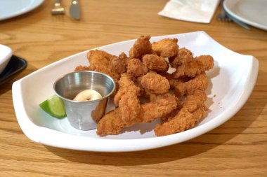 Panko ve Cajun soslu çıtır tavuk şeritleri bir restorandaki ahşap masada beyaz bir tepside.