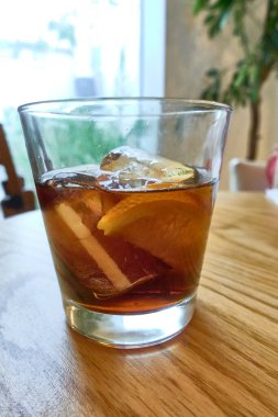 Soğuk sıvı, limon dilimi ve buzlu cam içinde vermut alkollü içecek. Lokantadaki ahşap masada ya da arka ışıklandırmalı evde.