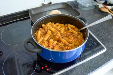 Blue pot with macaroni or rigatoni mixed with bolognese meat sauce on a home electric cooker ready to serve clipart