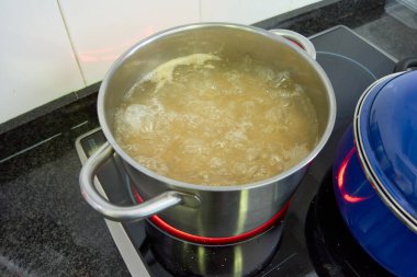 Büyük gümüş bir tencerenin üst görüntüsü makarna ile başka bir mavi tencere yanında bir ev mutfağında indüksiyon hob