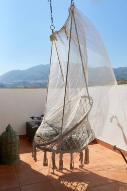 Beyaz sallanan hamak koltuğu balkonda asılı, arka planda muhteşem bir dağ manzarası, berrak bir gökyüzünün altında, rahatlama ve rahatlama için mükemmel bir yer oluşturuyor.