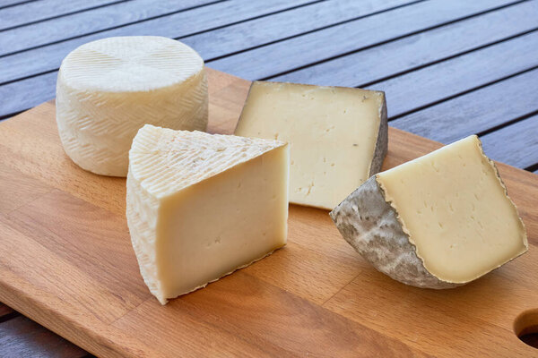 Wooden board with four wedges of artisan cheese. Each cheese has a different texture, rind, and color, suggesting a variety of flavors. Ideal for culinary or gourmet presentations