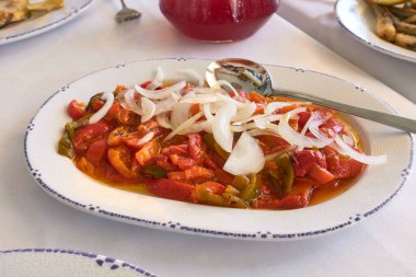 A traditional Spanish roasted pepper salad with sliced onions, served on a decorative white plate. The vibrant red peppers are dressed in olive oil and garnished with fresh onion rings clipart