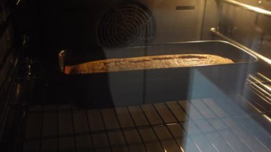 Bir somun ev yapımı ekmek ya da fırında kalıp yapan bir kek, cam kapıdan yakalanmış. Sıcak ışıklandırma, pişirme sürecinin gidişatını gösteren altın kahverengi kabuğu vurguluyor.