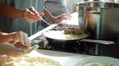 Kadın elleri, tencerede büyük bir tencerenin yanında ev yapımı köfteleri kızartıyordu. Onun yanında, bir kız un kaplı parmaklar yemeği şekillendirir.