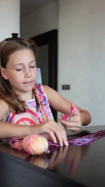 Oturma odasında oturan toptan makas kesen on bir yaşındaki bir kızın önü renkli yün ipliklerle kaplı. Dikey video