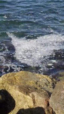 Kirlenmiş okyanusun su yüzeyindeki kirli köpüklerin dikey görüntüsü kayalık kirlenmiş sahil şeridinin yanında.