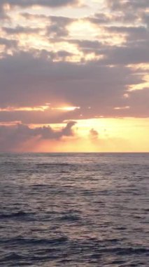 Deniz ufkunun üzerinde, altın saatinde kırmızı bulutlar arasında güneşin doğuşunu gösteren dikey video.