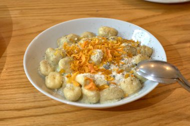 Adaçayı soslu Gnocchi makarna yanında tatlı patates gevreği, ahşap bir masada beyaz bir tabakta iki kaşık