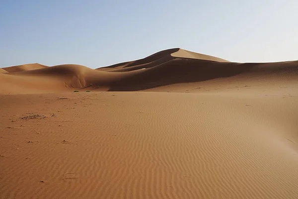 Afrika 'nın güneydoğusundaki Sahra Çölü' nde ıssız Erg Chigaga kum tepesi, Ocak 'ın sıcak ve güneşli 2023' ünde açık mavi gökyüzü..