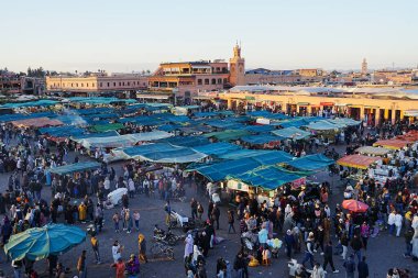 MARRAKESH, MOROCCO - 28 HAZİRAN 2023: Afrika 'nın Medine kentindeki Jemaa el-Fnaa çarşılarında turistler, ılık güneşli kış gününde açık mavi gökyüzü.