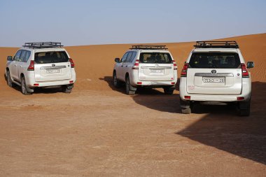 MHAMID EL GHIZLANE, MoroCCO 23 Ocak 2023: Afrika erg Chigaga kum tepesi yakınlarında üç off-road aracı, güneşli kış gününde açık mavi gökyüzü.