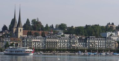 LUCERNE, SWitzERLAND - 6 AĞUSTOS 2018: Sıcak güneşli yaz gününde Avrupa 'da bir otel olan St. Leodegar' ın turistik tekne ve kilisesine bakın.