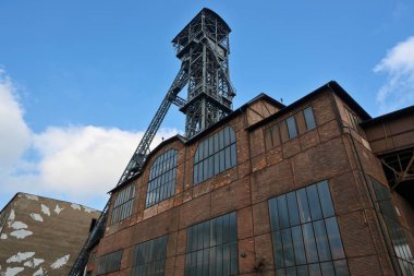 Historic coal mining tower and industrial buildings in Ostrava, Czech Republic. Bottom view of a brick building with tall windows and in the background with a steel mining tower.