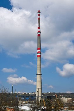 Arka planda bulutlu gökyüzü olan uzun bacalı sanayi bölgesi.