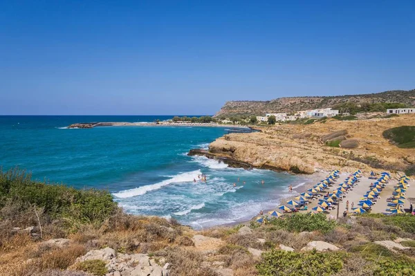 stock image Crete, Greece - August 19, 2019: Bay with a sandy beach with umbrellas and people bathing in a tourist resort on the island of Crete