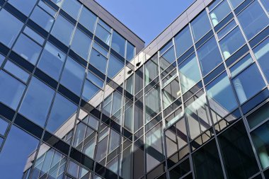 Pencerelerinde yansımalar, arka planında mavi bir gökyüzü olan modern bir ofis binasının ayrıntıları.