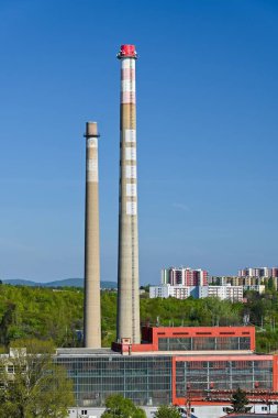 Endüstriyel binalarla manzara ve güneşli bir sabahta arka planda yerleşim alanı olan iki baca.