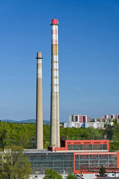 Endüstriyel binalarla manzara ve güneşli bir sabahta arka planda yerleşim alanı olan iki baca.