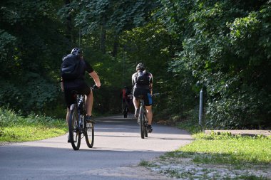 Brno, Çek Cumhuriyeti - 10 Ağustos 2022: Sabah güneşinde bisiklet süren bir grup erkek bir şehir parkında bisiklet sürüyor