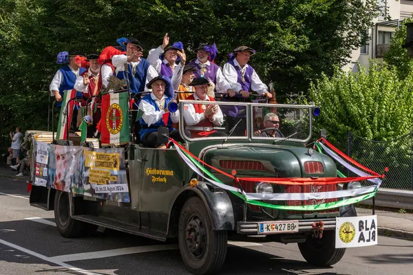 stock image Villach, Austria - August 03, 2024: A crowd of people wearing old city judges costumes riding on a old truck at the procession of 'Villacher Kirchtag', the largest traditional folk festival in Austria.