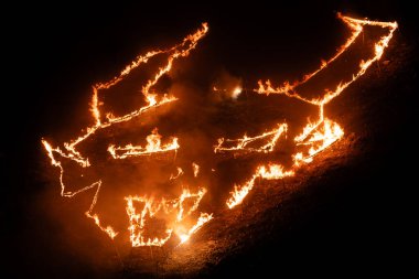 Fire paints a burning sign of the Krampus at a hill in the old mining town of Cave del Predil in Northern Italy clipart