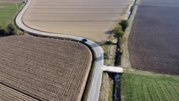 古い農場と太陽エネルギーパネルの間の農村部の道路を走行する青い車の空中ビュー — ストック動画