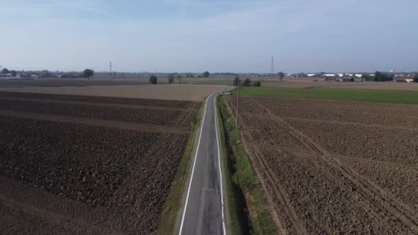 古い農場と太陽エネルギーパネルの間の農村部の道路を走行する青い車の空中ビュー — ストック動画