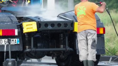 Adam, oto yıkamacıdaki self servis ekipmanlarını kullanarak mavi kamyonun dışını spreyliyor..