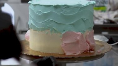 Pasta tasarımcısı, turkuaz açık mavi tereyağlı ve spatula 4K görüntülü buzlu pastayı yumuşatıyor.