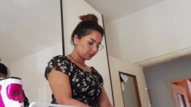 Genç, çekici bir ev kadınının video portresi. Ev işlerini ütülüyor.