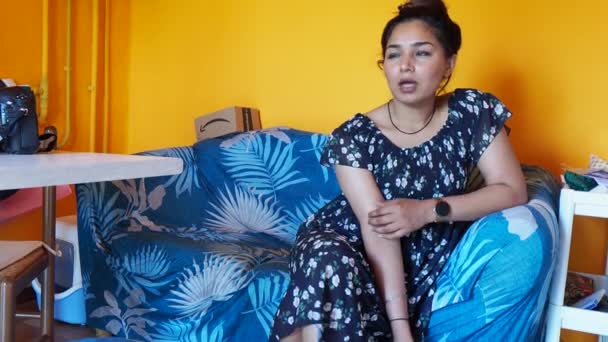 若いインド人の可愛い女性の映像を自宅のアパートのリビングルームでスマートフォンとチャット — ストック動画