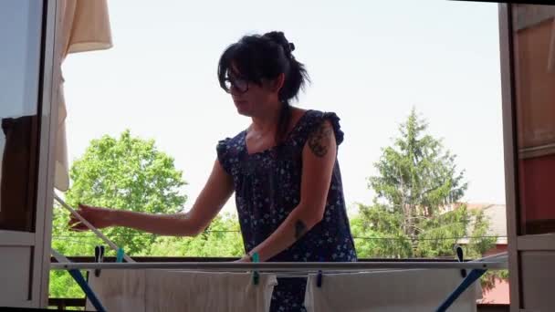 认真而有吸引力的40多岁的年轻女性 戴着眼镜 在家里的阳台上挂着新鲜的洗衣房 — 图库视频影像