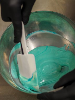 Pasta şefi pipo poşetini karıştırıyor. Renk derecelendirme için yenebilir turkuaz boyayla karıştırılıyor.
