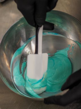 Pasta şefi pipo poşetini karıştırıyor. Renk derecelendirme için yenebilir turkuaz boyayla karıştırılıyor.