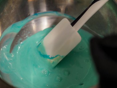 Pasta şefi pipo poşetini karıştırıyor. Renk derecelendirme için yenebilir turkuaz boyayla karıştırılıyor.